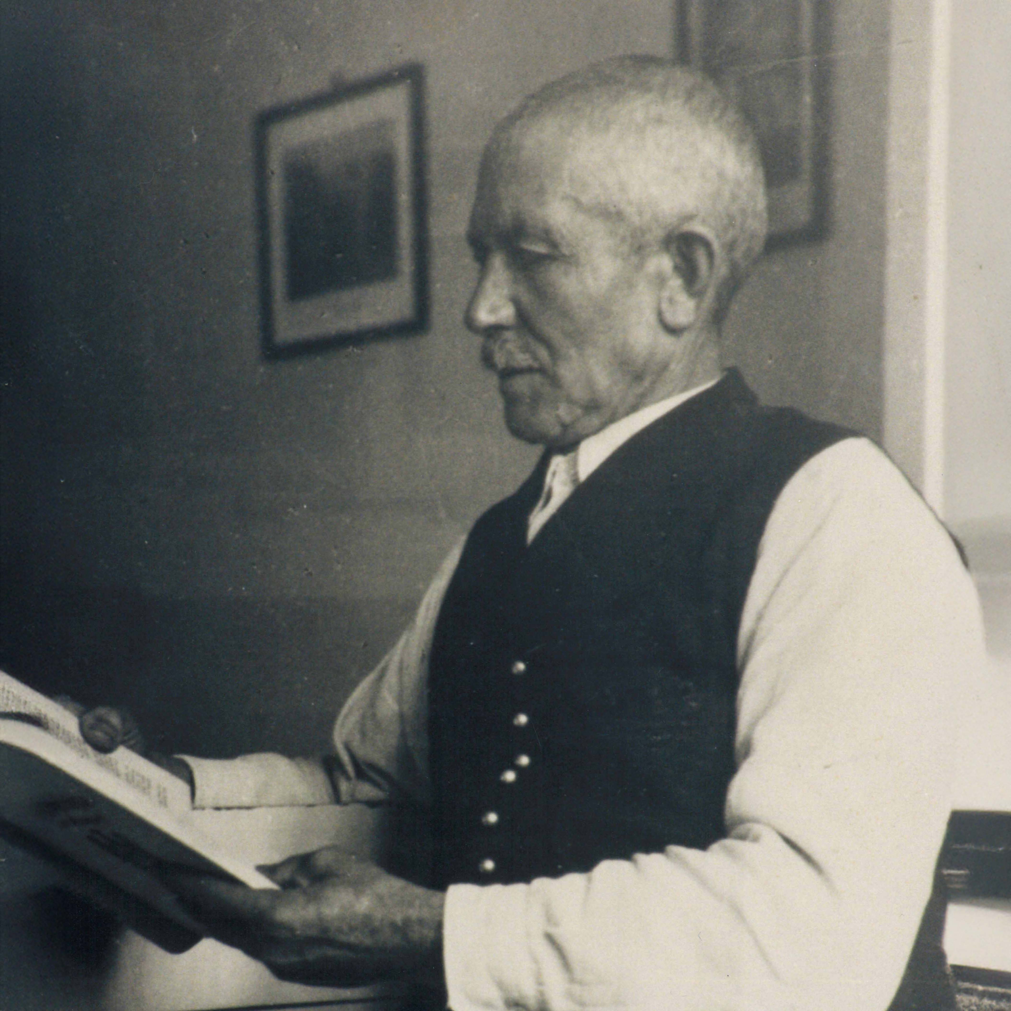 Porträt eines älteren Mannes mit kurzem Haar und Weste, der ein Buch liest.