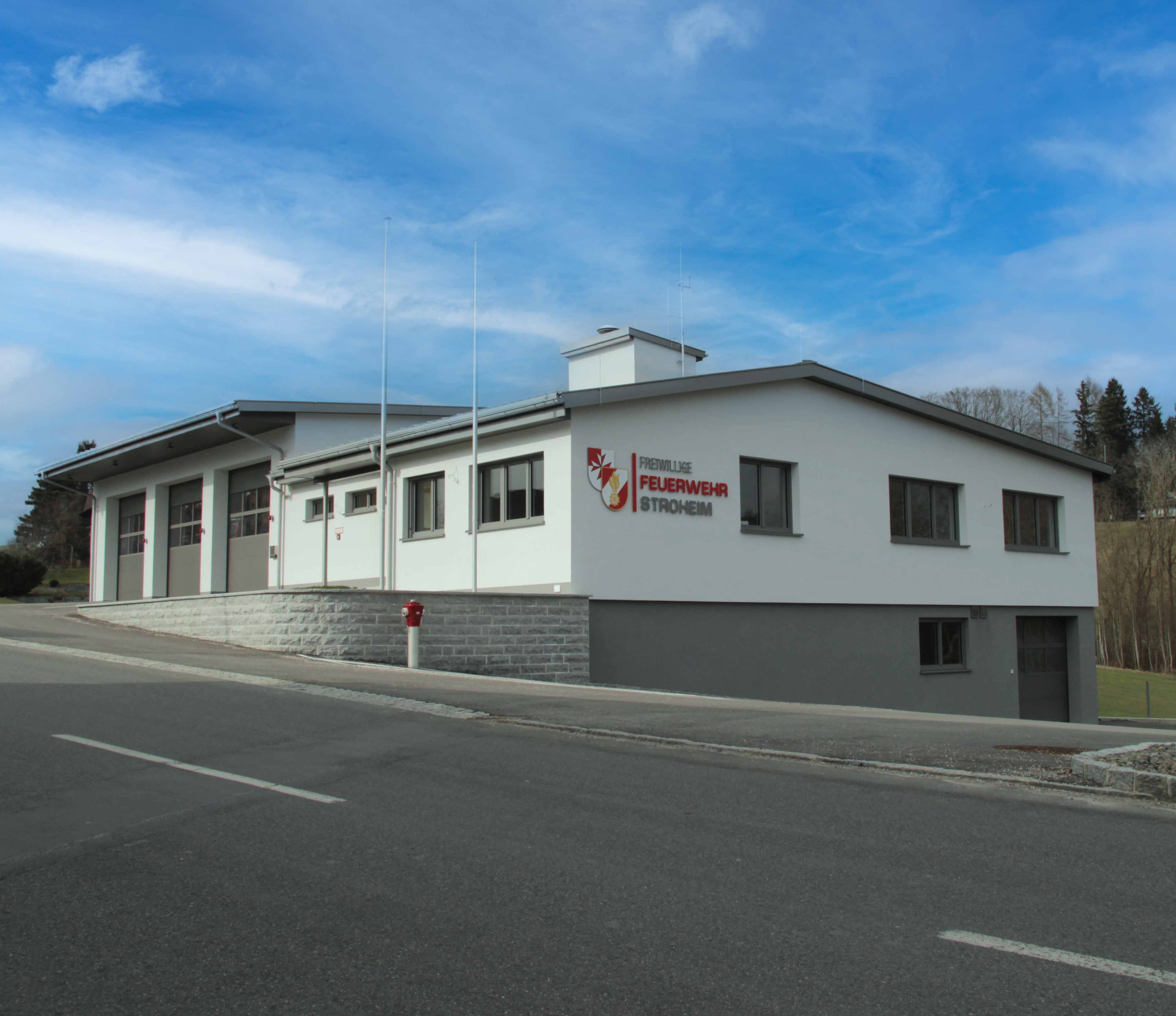 Modernes Gebäude der Freiwilligen Feuerwehr Stroheim mit mehrfarbigem Logo an der Fassade unter blauem Himmel.