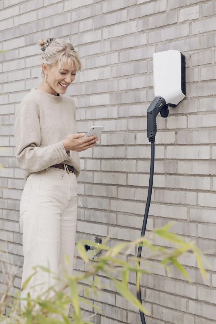 Ung kvinne står med mobil ved Easee Charge elbil lader