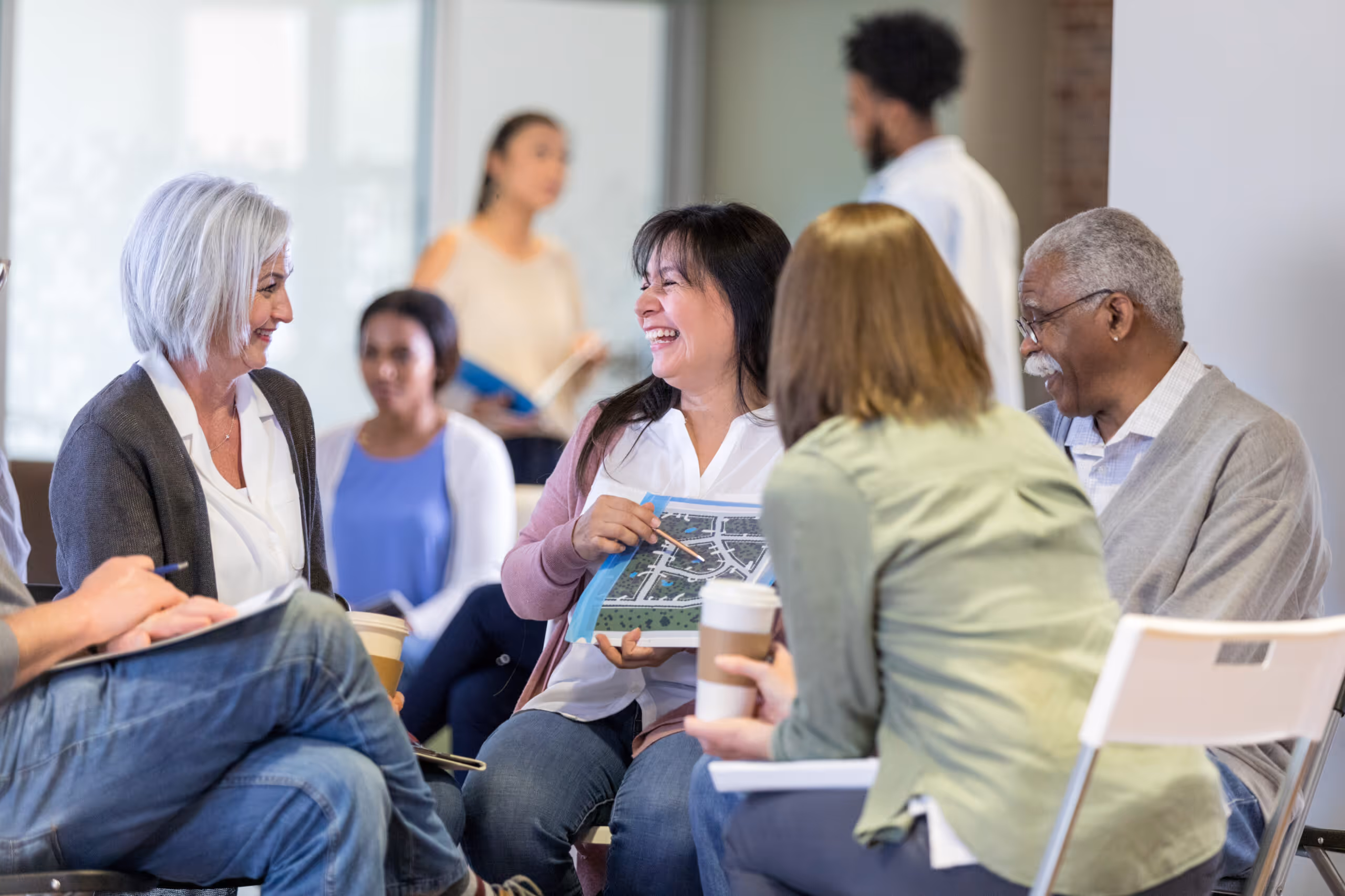 Diverse group of people seated in a circle, smiling and discussing a document with a map.
