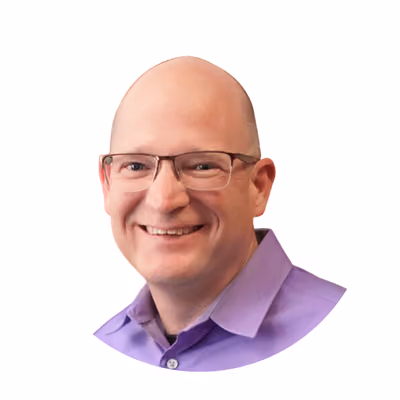Smiling bald man with glasses wearing a purple collared shirt against a white background.