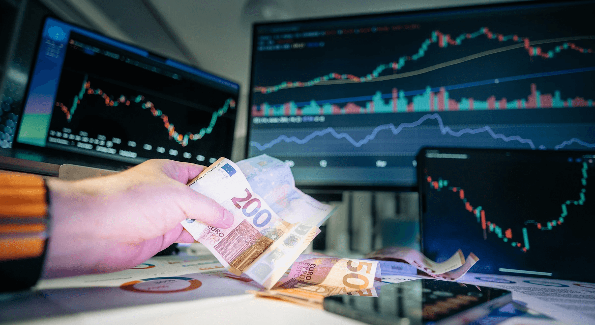 Person holding cash near trading monitors - Forex Trading Profit Per Day