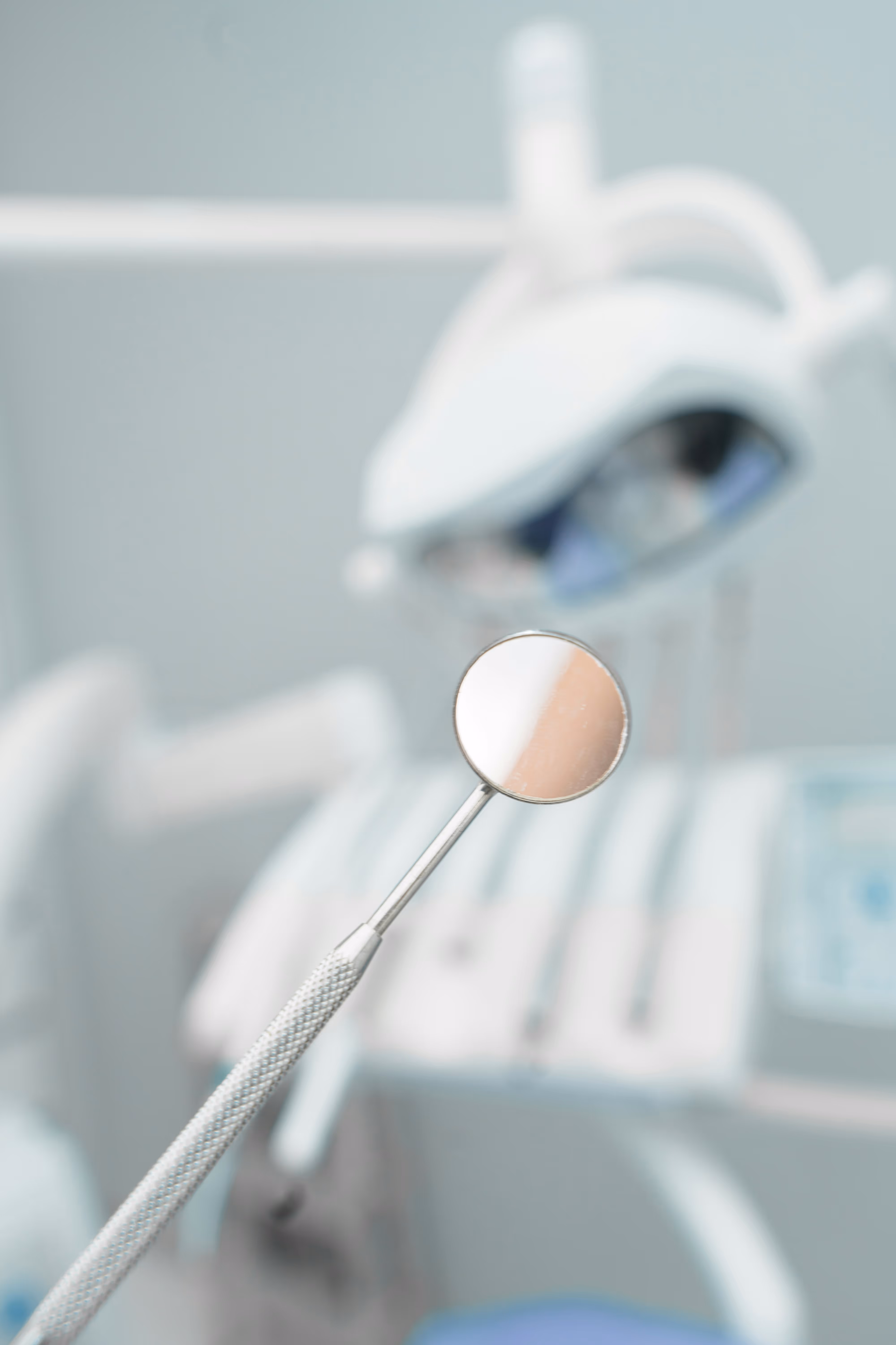 Close-up of a dental mirror with clinical tools blurred in the background, representing dental care, oral health examinations, or dental professional services.