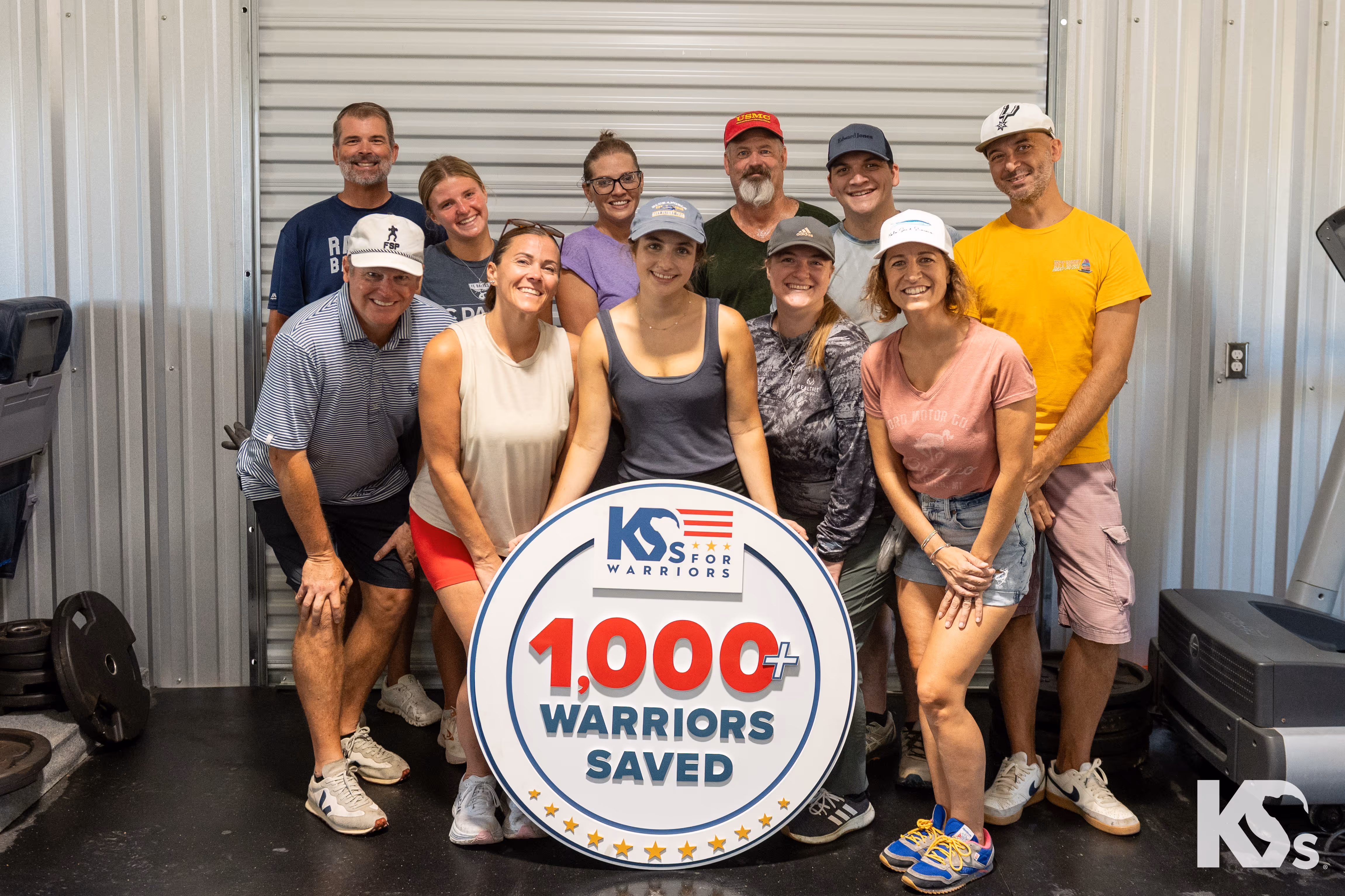 Group of K9s For Warriors supporters holding a sign reading “1,000+ Warriors Saved,” illustrating the organization’s impact in veteran rehabilitation through service dogs.