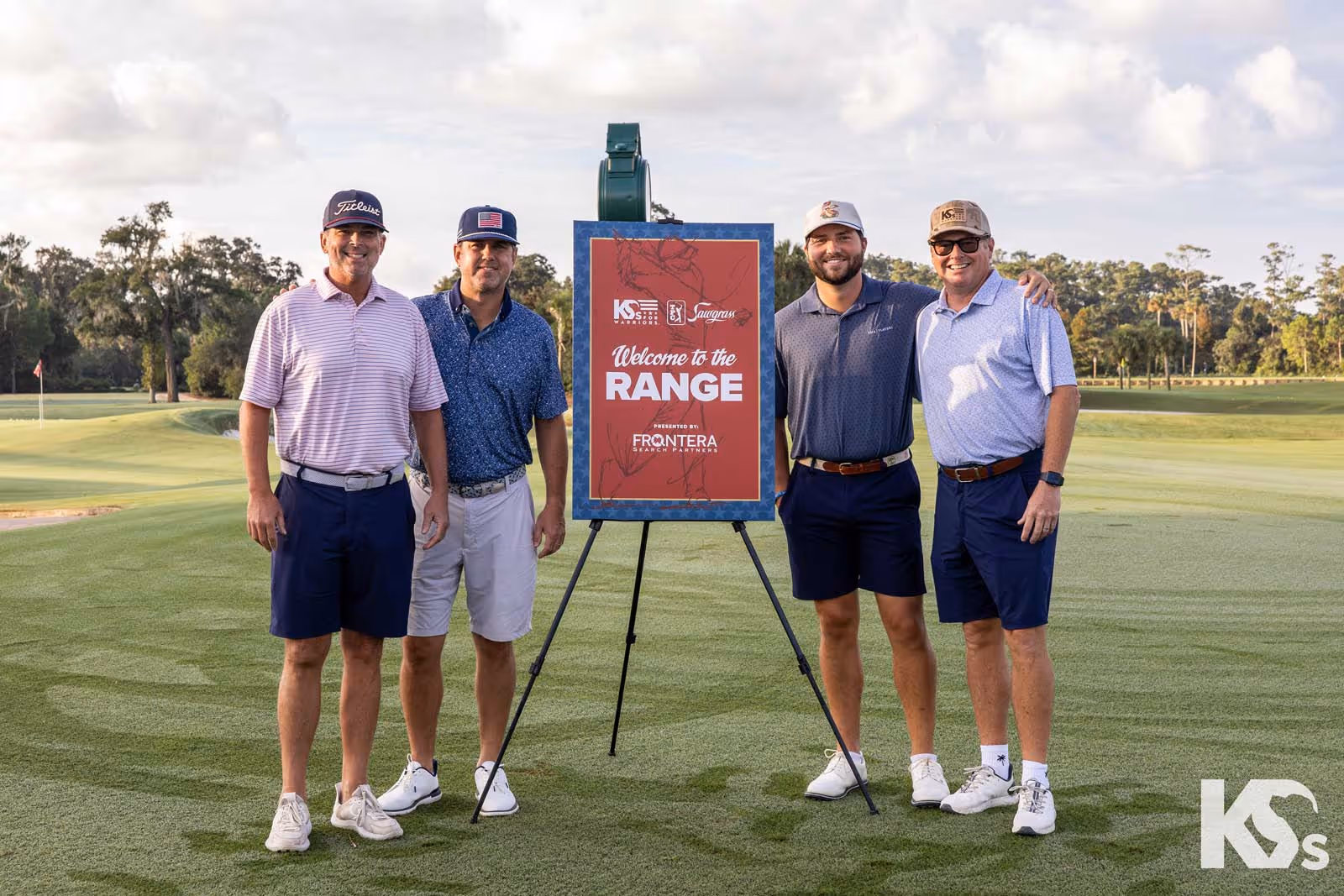 Group of men in golf attire standing on a golf course beside a sign reading “Welcome to the Range presented by Frontera Search Partners,” highlighting a sponsored networking or corporate event.