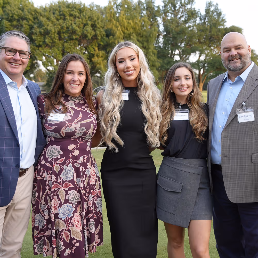 Five professionals standing outdoors in business casual attire, representing team collaboration and professional networking.