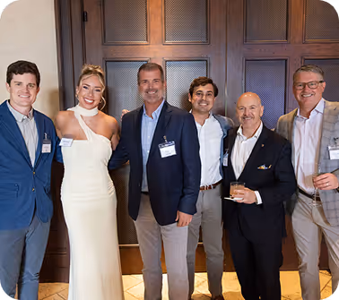 Group of professionals in formal attire posing indoors in front of wooden doors, illustrating leadership, partnerships, or corporate event participation.