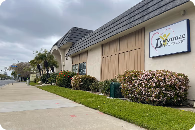 Exterior view of a clinic building with a sign reading 'Iestonnac Free Clinic' and landscaping along the sidewalk.