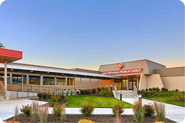 Saint Alphonsus Medical Center building with entrance, lawn, and clear sky at dusk.
