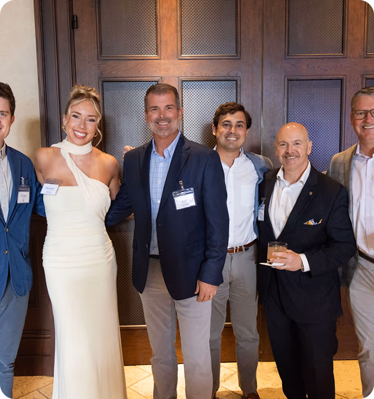 Five professionally dressed people smiling together at an indoor event, with a wood-paneled background.