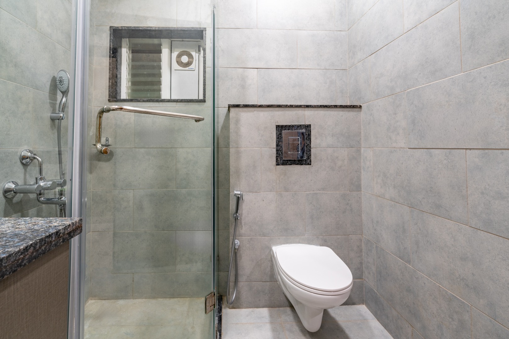 Luxury bathroom at Sri Narayana Vanam farmhouse featuring a walk-in glass shower, premium granite vanity, and modern grey tile finishes, offering a refreshing stay experience at a private farm stay in Aziznagar, Moinabad, Hyderabad, located at Survey No. 129. Contact: 998-994-1555.