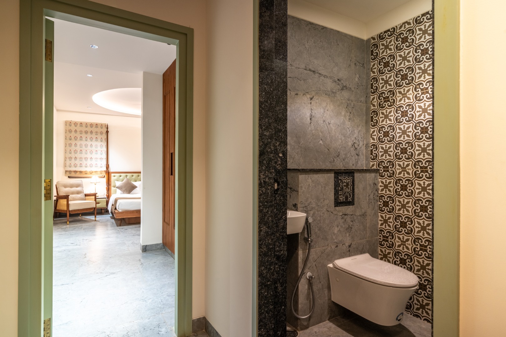 Elegant modern bathroom at Sri Narayana Vanam farmhouse featuring designer patterned tiles, premium stone finishes, wall-mounted WC, and refined interiors, viewed from a luxury bedroom, offering a private and comfortable stay at a premium farm stay and vacation rental in Aziznagar, Moinabad, Hyderabad, located at Survey No. 129. Contact: 998-994-1555.