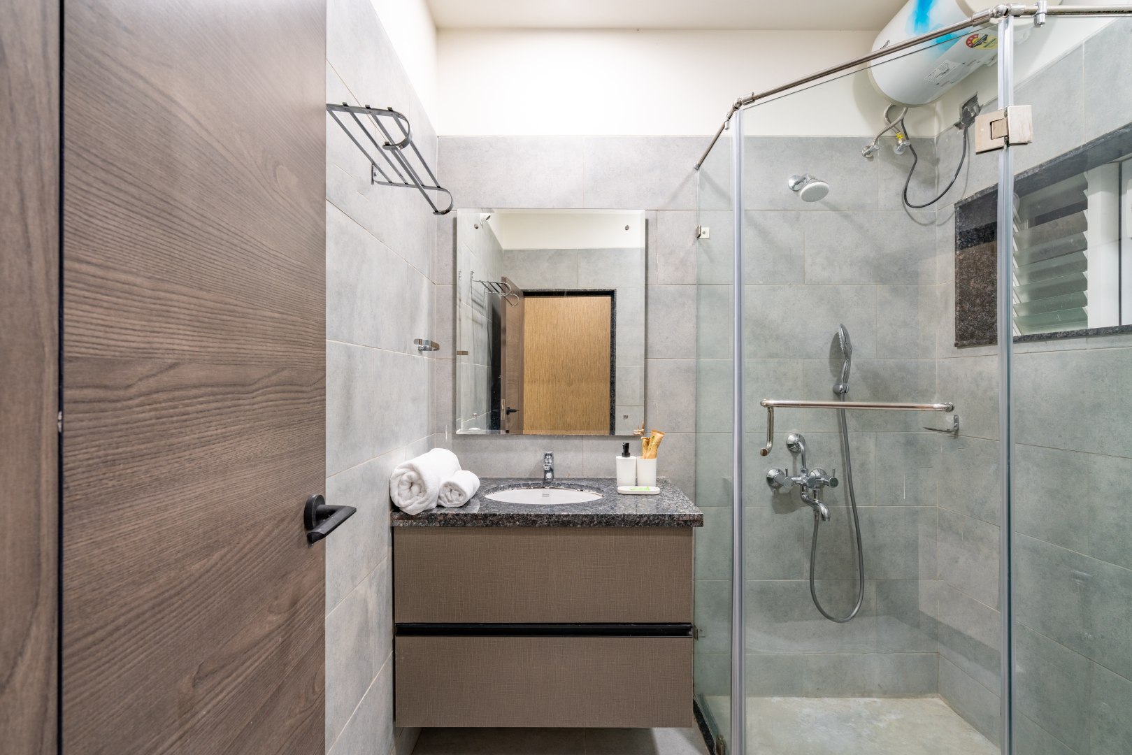 Contemporary luxury bathroom at Sri Narayana Vanam farmhouse showcasing a walk-in glass shower, premium granite vanity, modern sanitary fittings, and elegant neutral-toned tile finishes, designed for a relaxing and hygienic stay at a private farm stay and vacation rental in Aziznagar, Moinabad, Hyderabad, located at Survey No. 129. Contact: 998-994-1555.