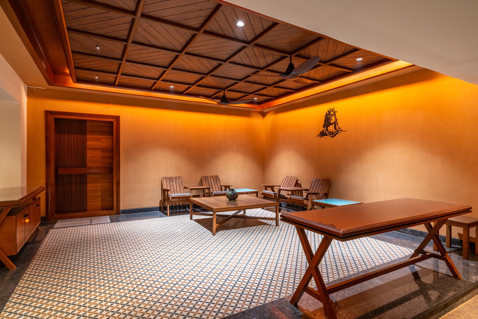 Warmly lit indoor lounge and gathering area at Sri Narayana Vanam farmhouse in Moinabad, Hyderabad, featuring a decorative wooden lattice ceiling, traditional seating, and a large patterned carpet at Survey number 129, Aziznagar, Telangana 500075.