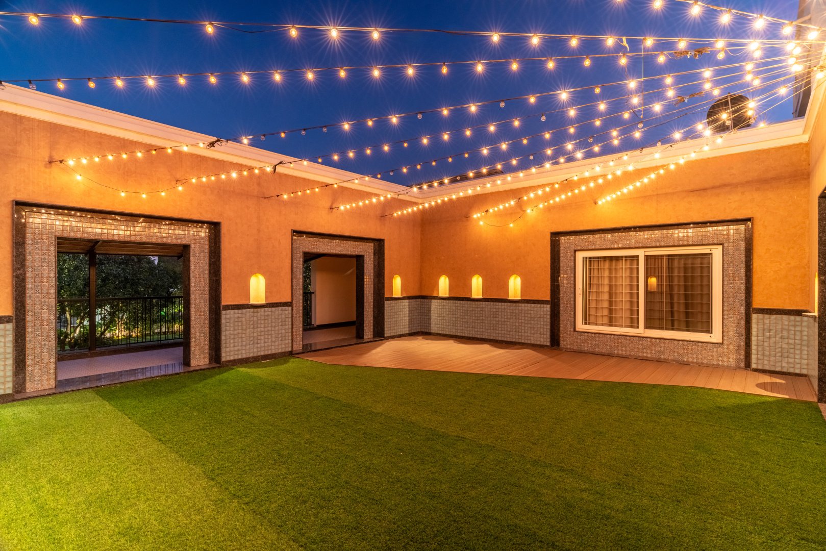 Illuminated rooftop event space at Sri Narayana Vanam farmhouse in Moinabad, Hyderabad, featuring premium artificial turf, warm fairy light strings, and elegant wall-mounted lamps at Survey number 129, Aziznagar, Telangana 500075.