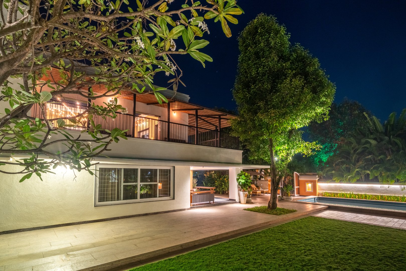 Night view of the luxury two-story villa at Sri Narayana Vanam farmhouse in Moinabad, Hyderabad, featuring an illuminated swimming pool, spacious balcony, and lush green lawns at Survey number 129, Aziznagar, Telangana 500075.