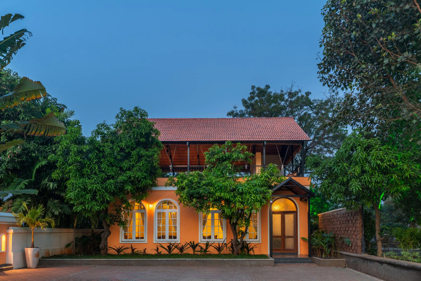 Exterior view of a charming holiday cottage guest room at a private luxury farm stay. This boutique retreat features warm lighting, classic arched windows, and lush greenery at Survey number 129, Moinabad Mandal, Aziznagar, Hyderabad, Telangana 500075. An ideal vacation rental for couples seeking peace and privacy.