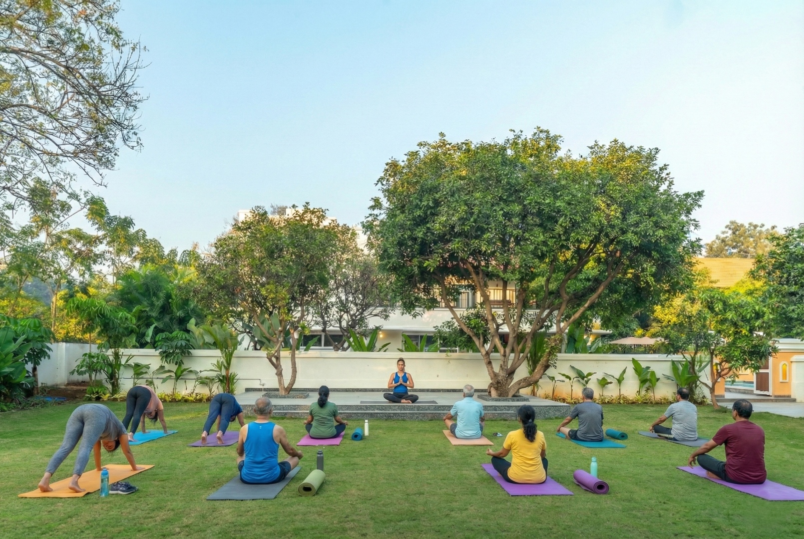 Outdoor wellness session at Sri Narayana Vanam farmhouse, featuring a group yoga class on a lush, manicured lawn surrounded by mature trees. Located at Survey number 129, Moinabad Mandal, Aziznagar, Hyderabad, Telangana 500075. This serene environment is ideal for wellness retreats, morning fitness sessions, and peaceful outdoor activities during a luxury farm stay.