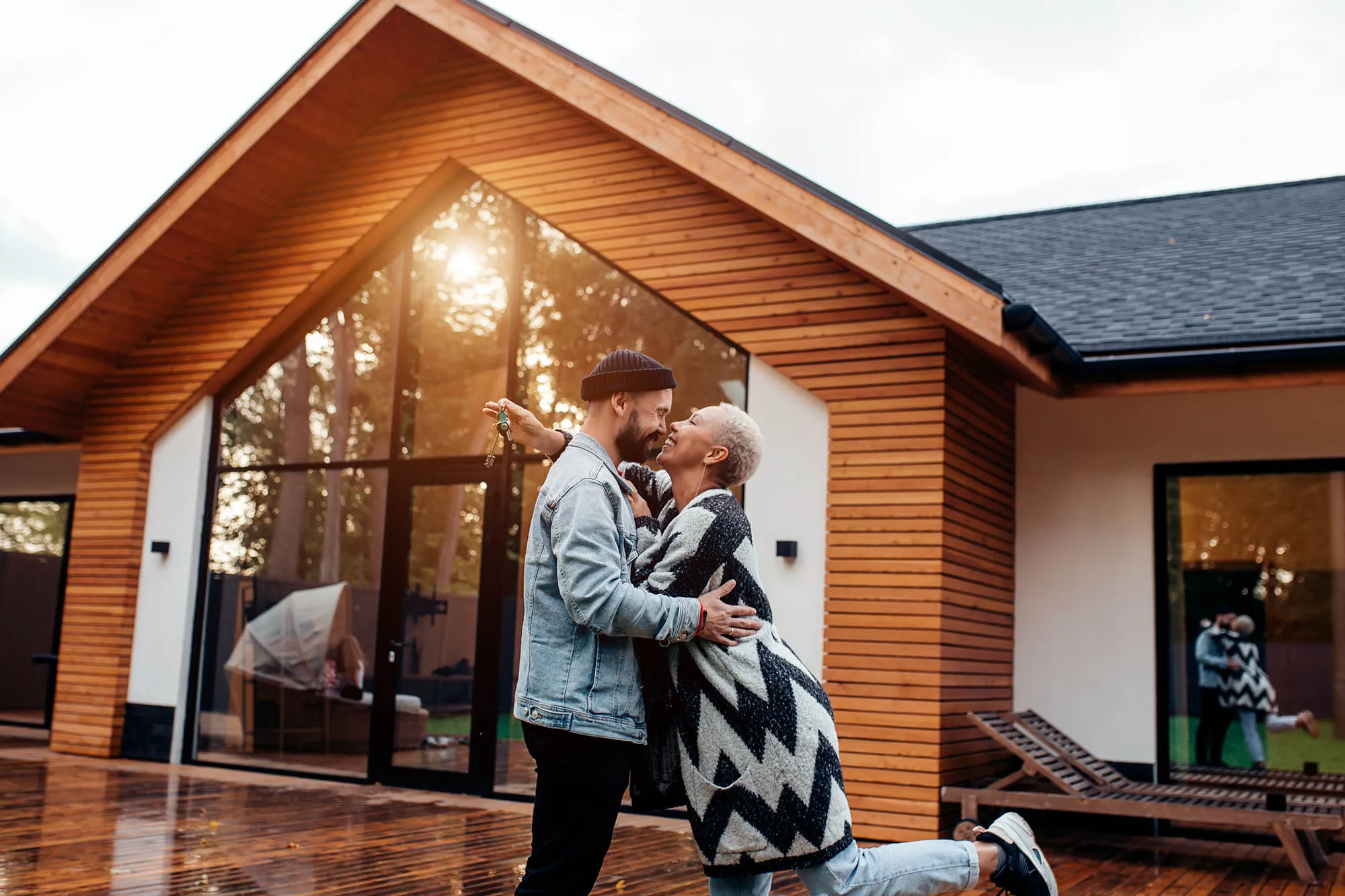 Ein Paar umarmt sich vor einem modernen Holzhaus, während der Mann einen Schlüssel anhält.