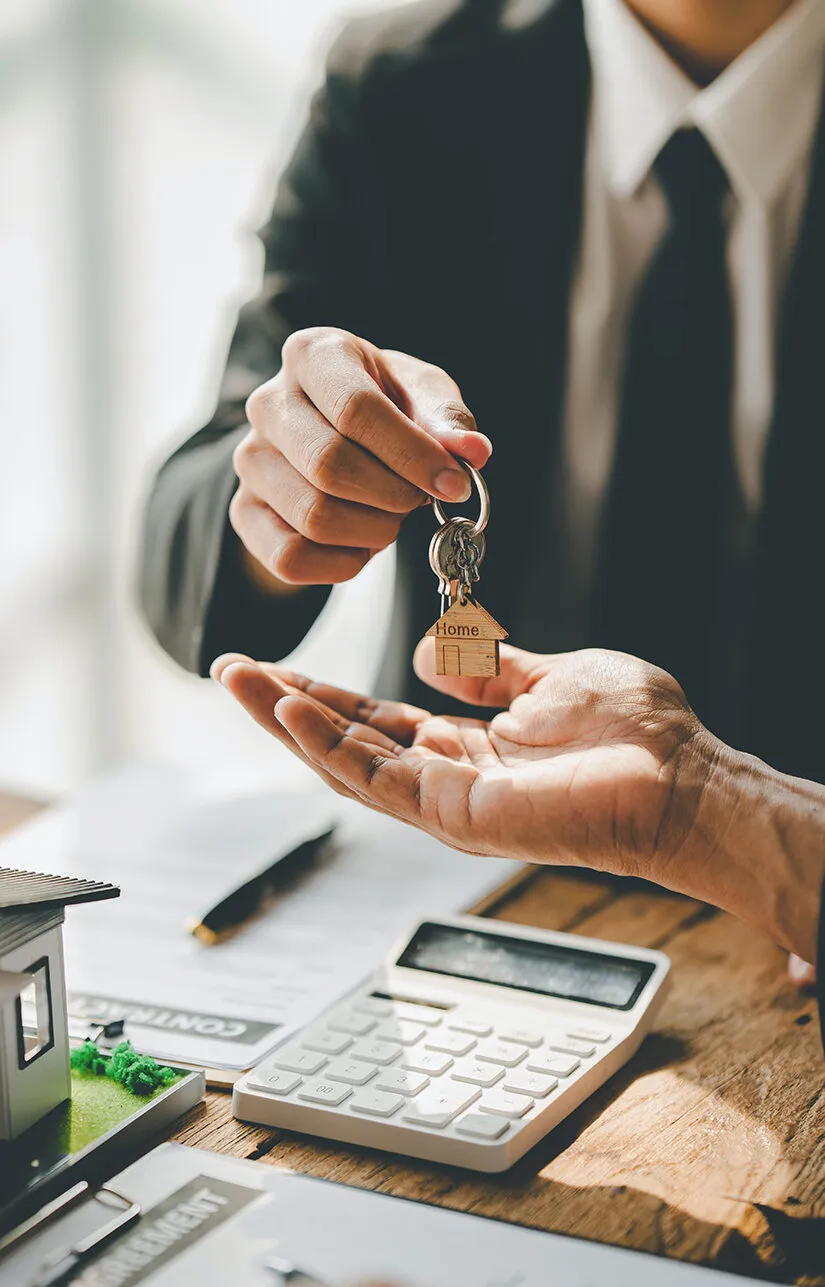 Eine Person in Anzug übergibt einen Schlüssel mit Hausanhänger an eine andere offene Hand.
