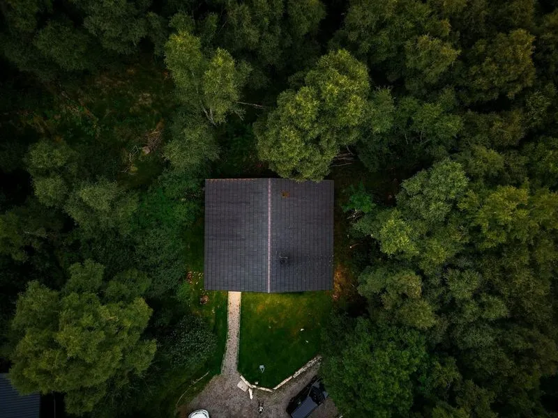 Aerial view of a dark-roofed house surrounded by lush green trees and a stone pathway leading to it.