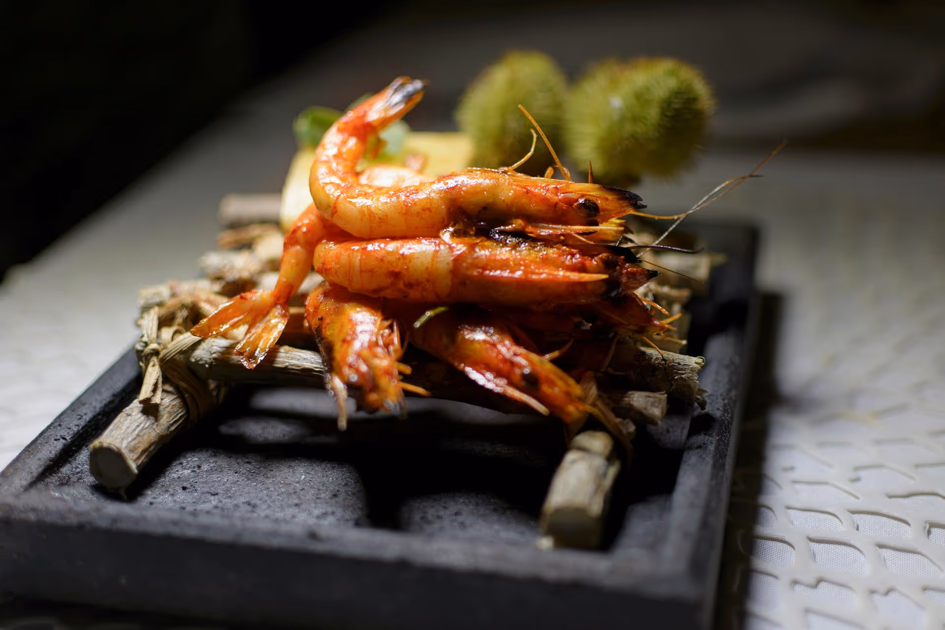 Grilled prawns artfully arranged on a black stone plate, garnished with herbs, showcasing vibrant colors and textures.