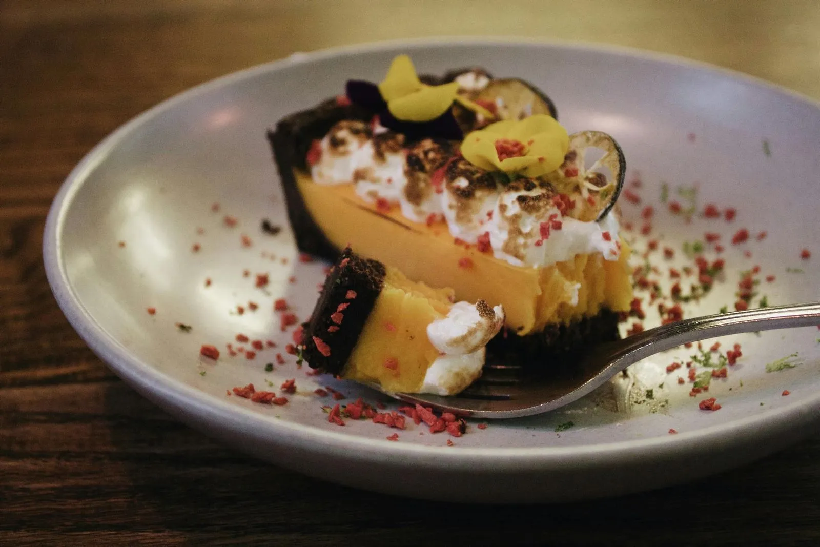 Delicious dessert served in a bowl, featuring creamy layers topped with nuts, chocolate drizzle, and colorful sprinkles. Spoon resting beside.