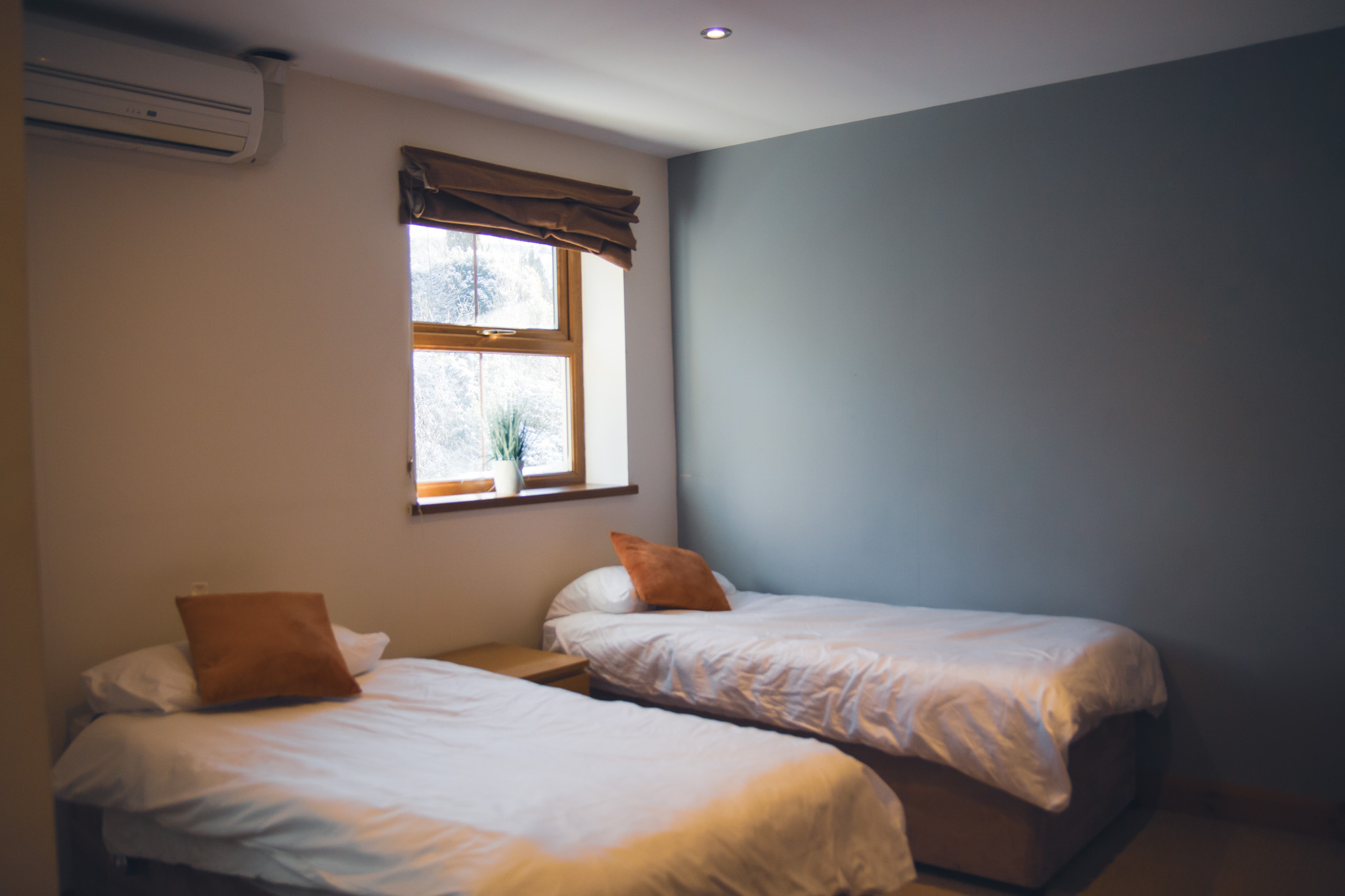 A modern blue house nestled among lush green trees and hills under a cloudy sky, surrounded by tranquil nature.