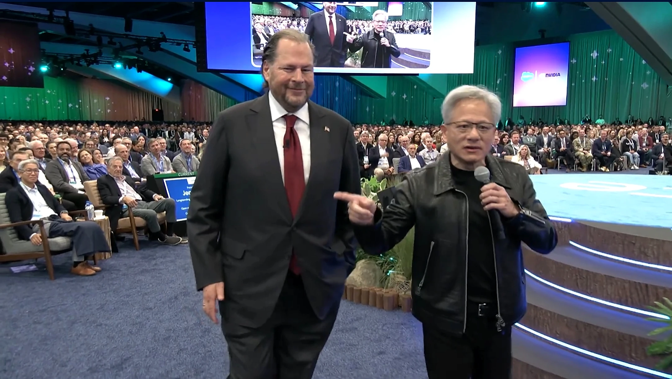 Two speakers on the Dreamforce 2026 main keynote stage in front of a Salesforce and NVIDIA screen, one pointing at the other while speaking into a microphone.