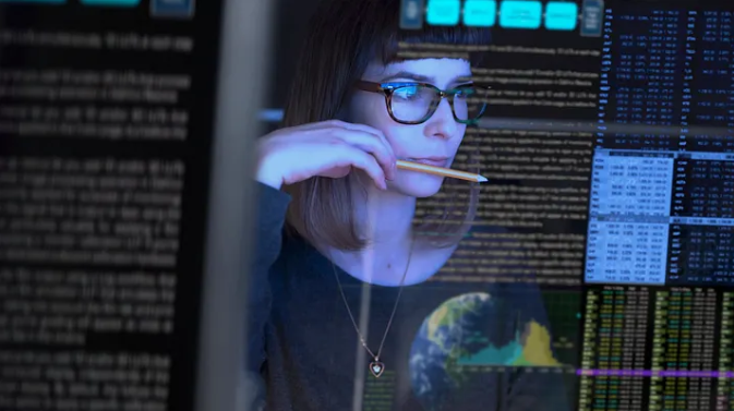 Photo of a woman studying overlaid data and code visualizations while holding a pencil