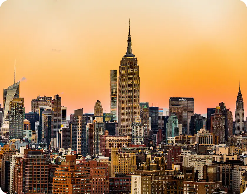 New York City skyline at sunset with the Empire State Building prominently in the center against an orange sky.