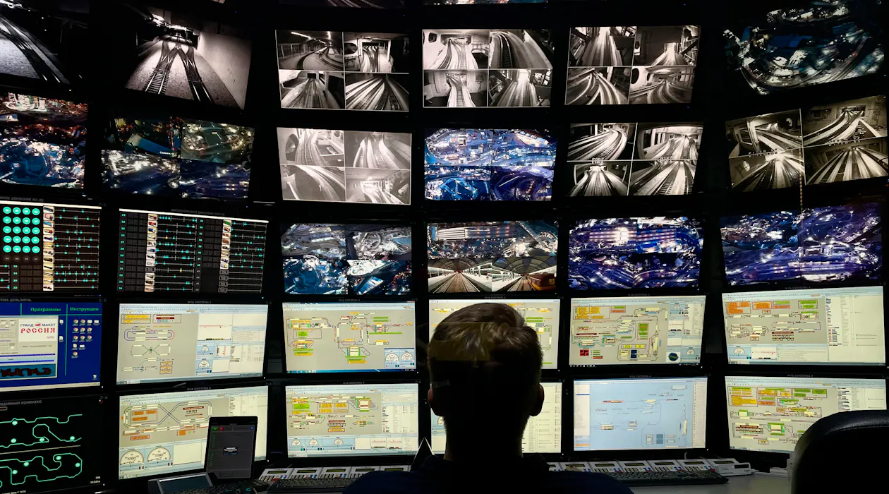 IT operator facing a wall of monitoring screens in an operations center