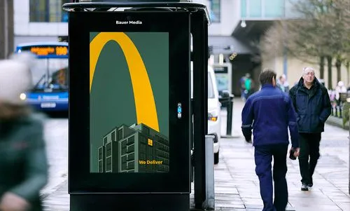 Pedestrians walk by a digital screen located at a bus shelter