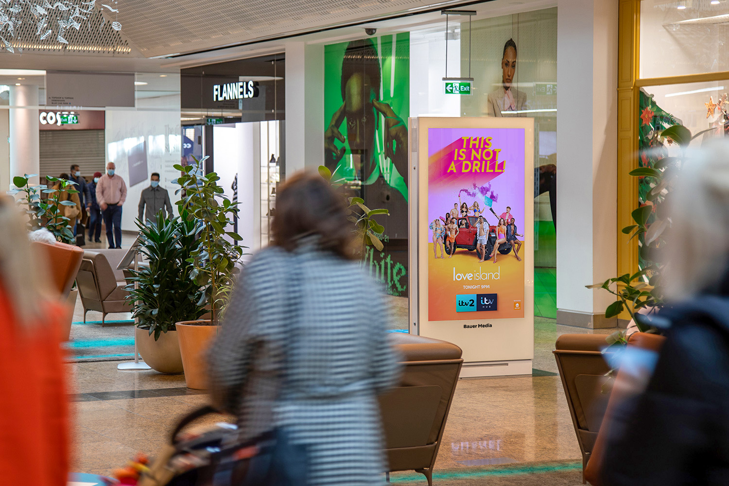 Shoppers passing through a shopping centre with a digital screen as the focal point