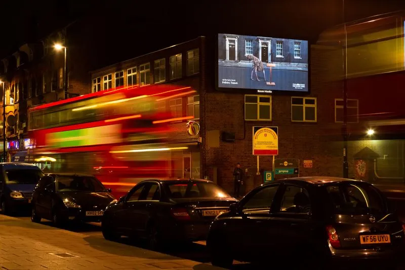 Digital billboard on the side of a building at nighttime as a bus drives by
