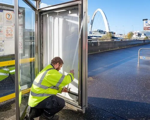 A Bauer Media Outdoor male construction worker installing LED lights in an Adshel panel