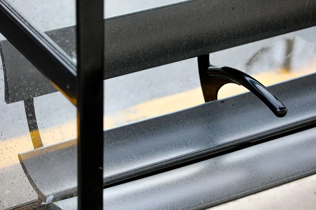 A zoomed image of a black bus shelter seat with an arm rest