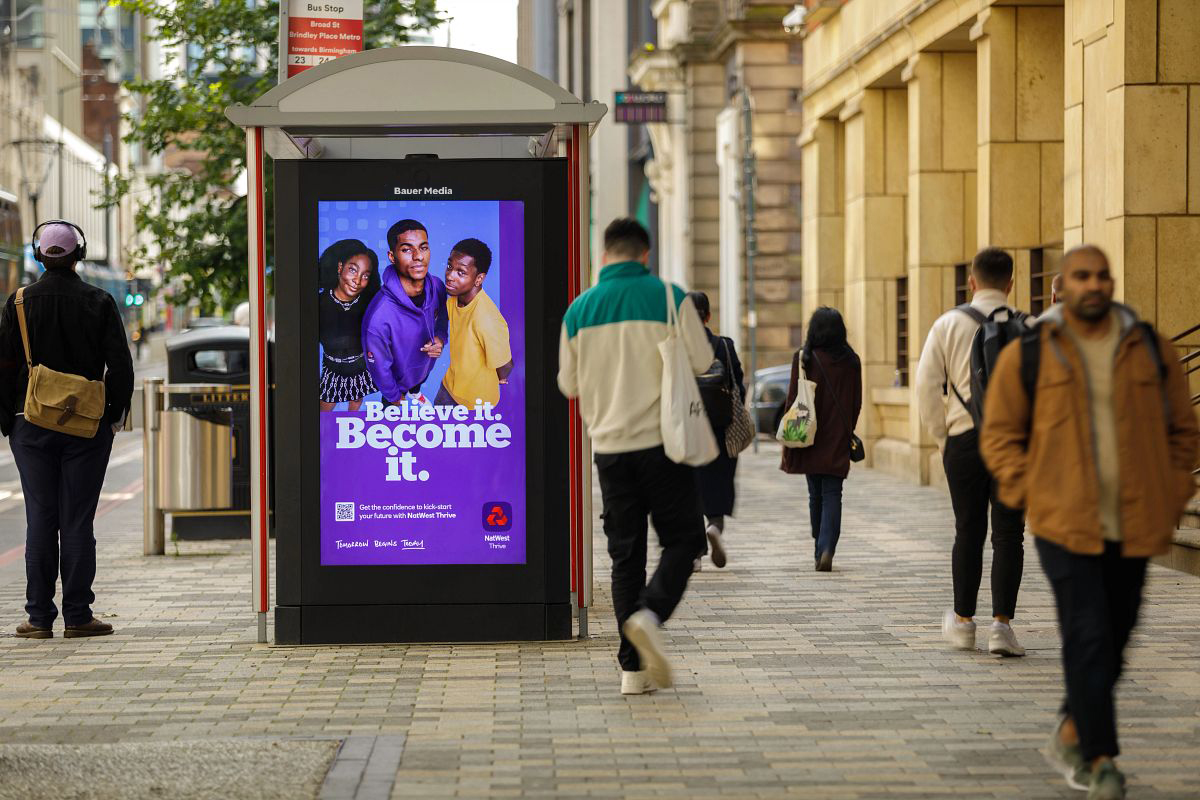 A Natwest advert on a high street digital screen with people walking by