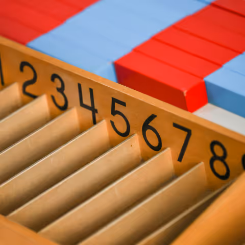 Wooden board with numbered slots 1 to 8 and red and blue counting blocks in the background.