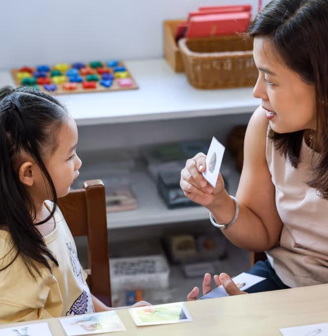 Woman showing a flashcard to a young girl sitting at a table learning together indoors.