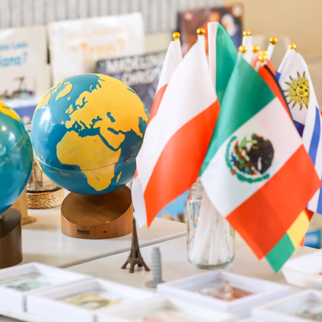 Small globes showing continents on wooden stands with several miniature international flags, including Mexico and Poland, displayed in glass jars on a white table.