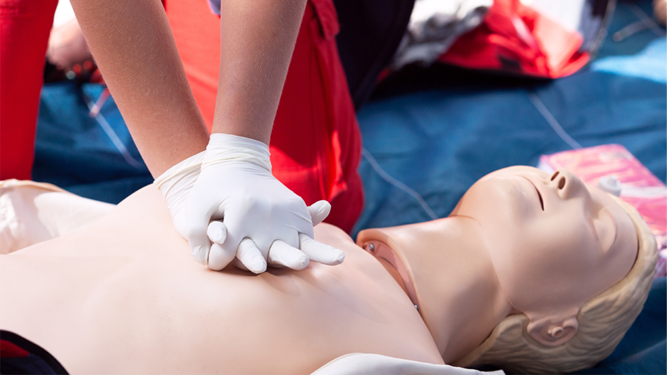 Person wearing gloves performing CPR chest compressions on a training manikin.