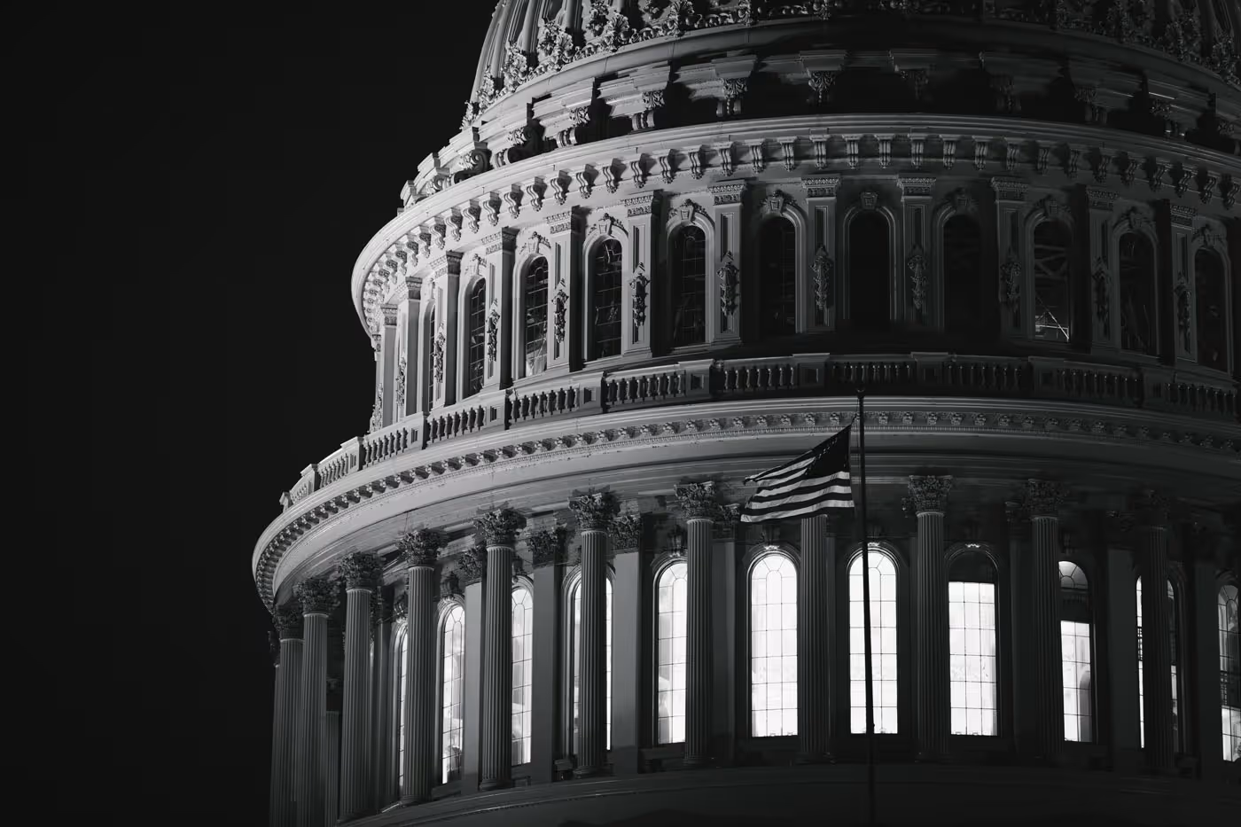 Close-up of the illuminated dome of a neoclassical building at night with an American flag in front.