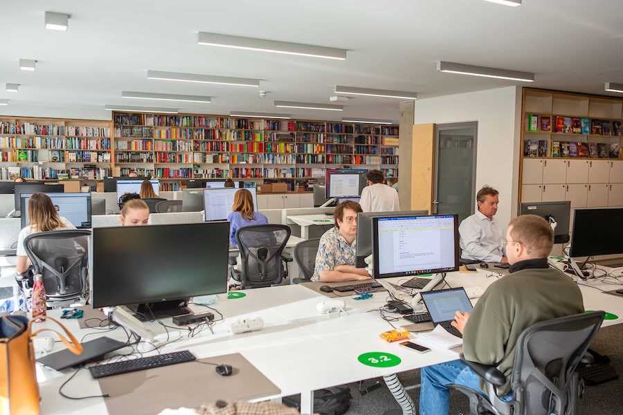 Pan Macmillan office, employee working on their computers surrounded by shelves of books. 