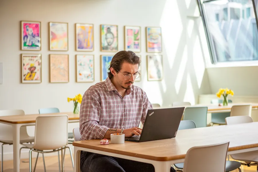 Male Pan Macmillan employee working in a warmly lit office space with large windows. 