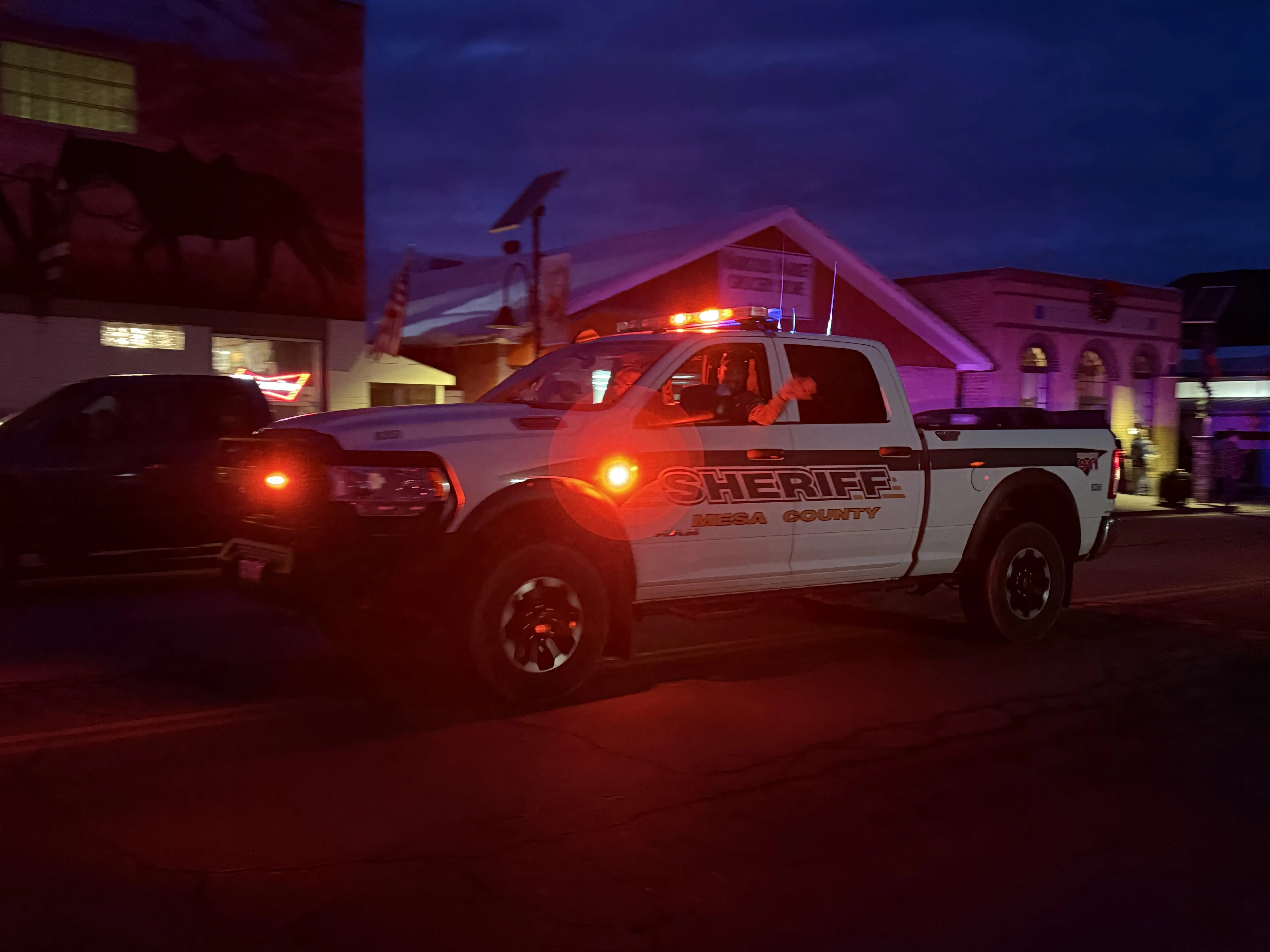 Mesa County sheriff's white pickup truck with flashing lights driving on a street at dusk.