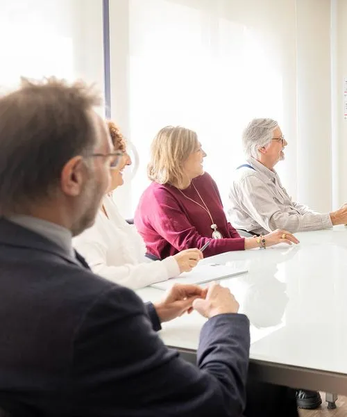 Cuatro adultos mayores sentados en una mesa blanca en una reunión o discusión.