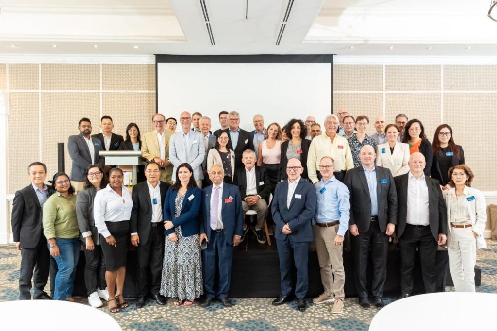 Grupo grande de personas posando en sala de conferencias frente a una pantalla blanca.