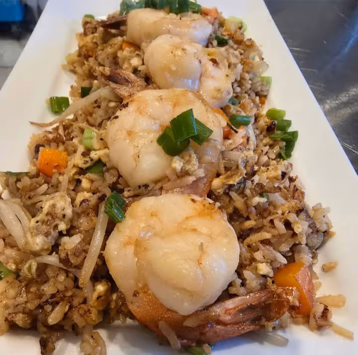A plate of shrimp fried rice garnished with green onions. The rice includes mixed vegetables and eggs, creating a colorful and appetizing display.