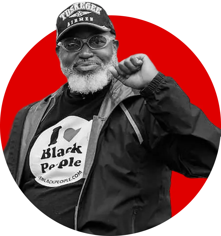 Man with glasses and white beard wearing a cap and a jacket, raising his fist in front of a red circle.